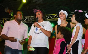 Claudia Ferreira, da Associação Grupo Cultural Nosso Ritmo. Na foto, ela está em um palco, falando no microfone, com alguns jovens ao lado.